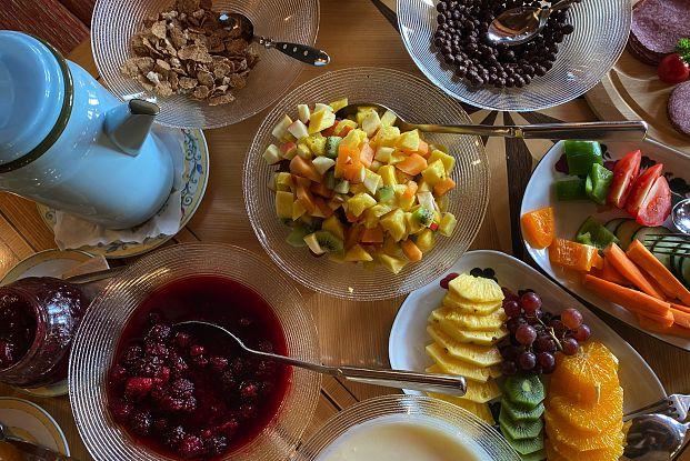 Eine bunten Auswahl an frischen Früchten in Schalen, darunter Melonen, Ananas und Beeren. Dazu befinden sich Müsli und Getränke in der Mitte des Tisches.