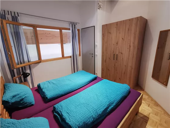 Ein gemütliches Schlafzimmer mit zwei Einzelbetten in lebhaften Farben. Der Raum hat ein Fenster mit Vorhängen und einen Holzschrank an der Wand.