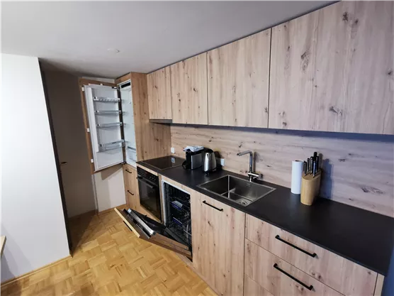 Eine moderne Küche mit Holzfronten und einem schwarzen Arbeitsfeld. Der Kühlschrank ist geöffnet und die Küchengeräte sind ordentlich angeordnet.