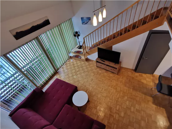 Ein modernes Wohnambiente mit einem roten Sofa und einem runden Tisch. Große Fenster lassen viel Licht herein und bieten einen Blick auf eine Holztreppe.