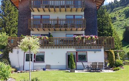 Ein schönes Haus mit mehreren Balkonen und einer gepflegten Gartenlandschaft. Die Umgebung ist von Bergen umgeben und strahlt Ruhe aus.