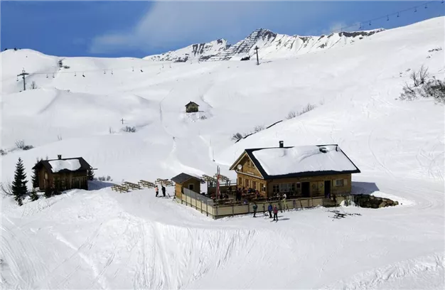 A mountain hut in snowy terrain, surrounded by mountains. Skiers enjoy the winter landscape.