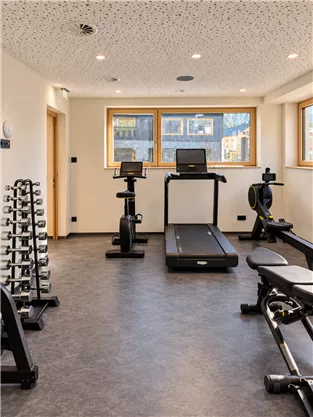 A modern gym with a treadmill, bike, and various dumbbells. Large windows provide natural light and a pleasant atmosphere.