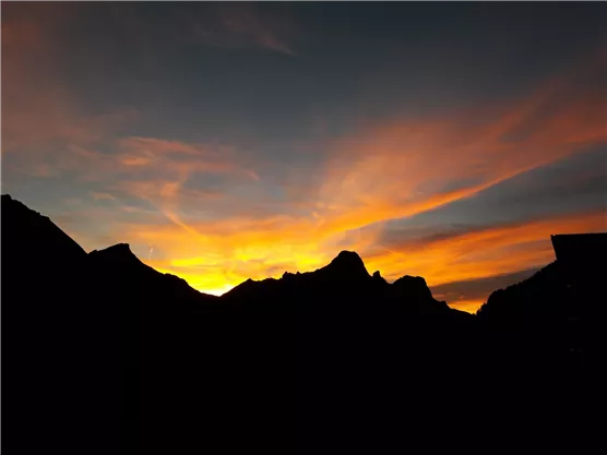 Ein beeindruckender Sonnenuntergang hinter Bergen. Die Himmelshorizont strahlt in warmen Orange- und Gelbtönen.