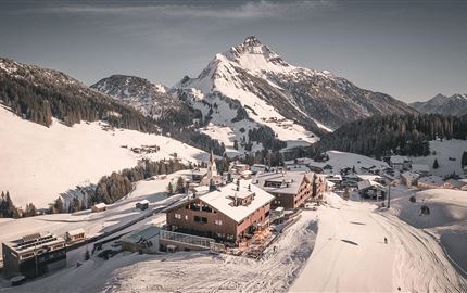 Eine malerische Berglandschaft mit schneebedeckten Hügeln. Im Vordergrund befindet sich eine gemütliche Berghütte.