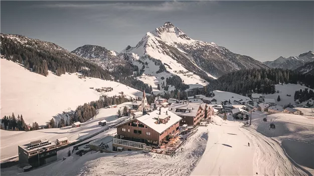 A picturesque mountain landscape with snowy hills. In the foreground is a cozy mountain cabin.