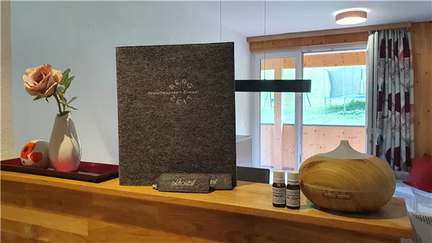 A stylish living area with a decorative vase and a beautiful rose. On the wooden surface, there are essential oils and a diffuser.