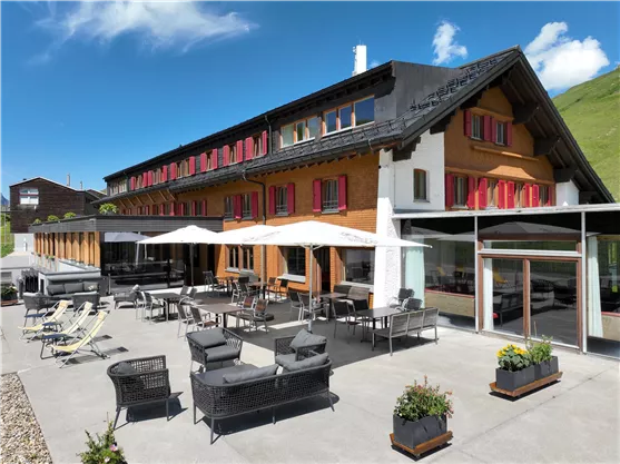 Ein modernes Hotel mit einem einladenden Außenbereich. Die Terrasse ist mit stilvollen Möbeln und Sonnenschirmen ausgestattet, umgeben von grünen Hügeln.