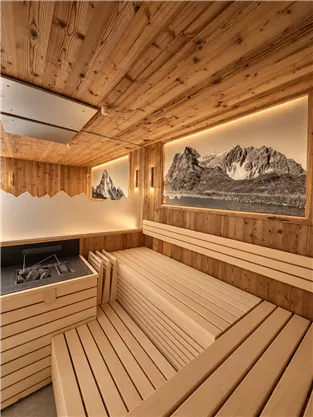 A modern sauna with bright wooden details and soft lighting. Impressive mountain photos hang on the walls.