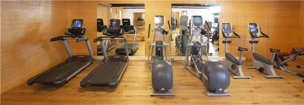 Ein modernes Fitnessstudio mit verschiedenen Trainingsgeräten. Die Wände sind aus Holz und die Atmosphäre ist hell und einladend.