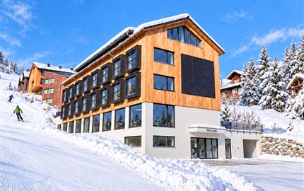 A modern hotel in a snow-covered landscape. The sky is blue and the slope is well-groomed.