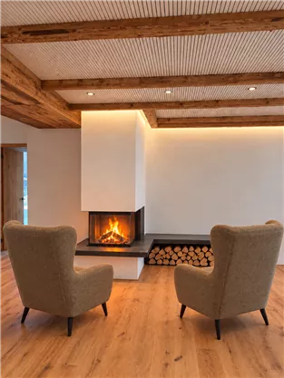 A cozy room with two armchairs and a modern fireplace. The wooden ceiling and floor create a warm atmosphere.