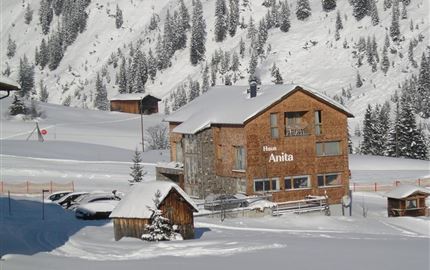 Ein gemütliches Holzhaus steht im Schnee, umgeben von verschneiten Bergen. Die Landschaft ist winterlich und friedlich.