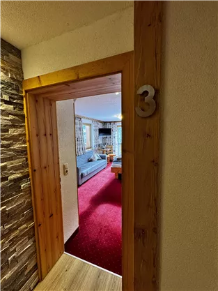 A hallway with room door number 3, leading to a cozy living space. The floor is covered with red carpet and the room has bright furniture.