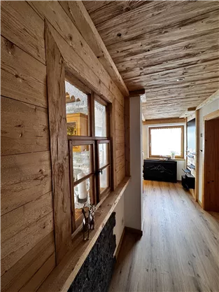 A cozy hallway with wooden walls and a wooden ceiling. Natural light enters the room through the windows.