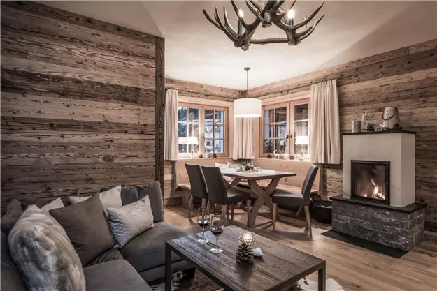 A cozy living room with wooden walls and a modern fireplace. The room is stylishly furnished with a comfortable sofa and a dining table.