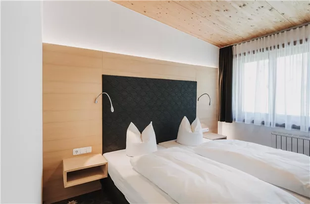 Ein modernes Schlafzimmer mit zwei Einzelbetten und einem dunklen Kopfteil. Die Wände sind hell, und große Fenster lassen viel Licht herein.