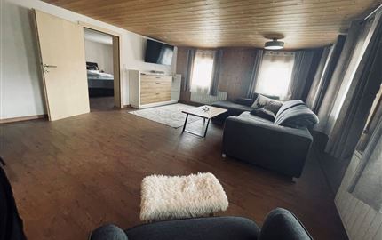 Ein gemütliches Wohnzimmer mit modernen Möbeln und hellem Holzdecke. Große Fenster sorgen für viel Tageslicht.