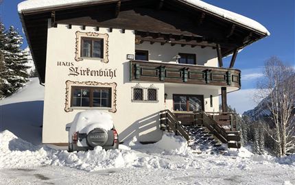 A snow-covered house named "Birkenbühl" in a winter landscape. The sky is blue and clear.