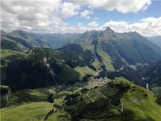 A picturesque mountain landscape with green meadows and steep peaks. The clear sky creates a peaceful atmosphere.