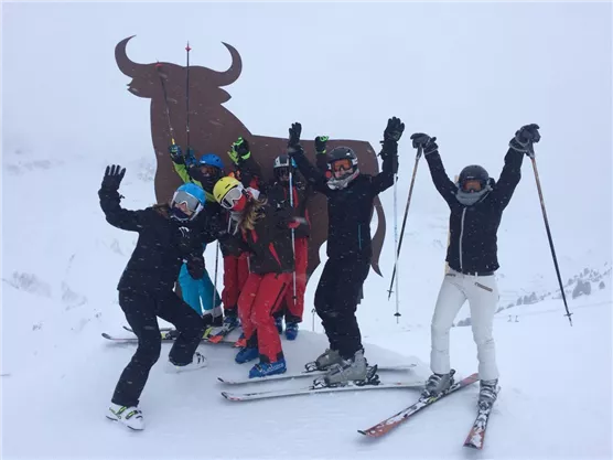 A group of skiers happily poses in the snow. In the background, a large statue of an animal can be seen.