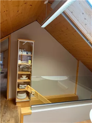 A bright, open space with a sloped ceiling and wooden paneling. In the background, there is an elegant shelf with dishes.