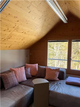 A cozy room with an L-shaped couch and cushions in soft colors. Large windows offer a nice view outside.