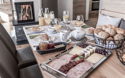 Ein schön gedeckter Tisch mit einer Auswahl an Frühstückslebensmitteln und Getränken. Im Hintergrund brennt ein Kamin.