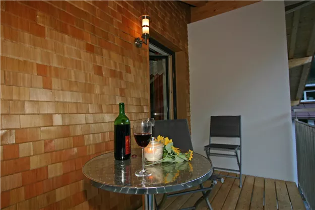 Ein gemütlicher Balkon mit einem runden Tisch, einer Flasche Wein und einem Glas. Im Hintergrund sind Holzverkleidungen und ein Stuhl sichtbar.