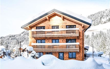 Ein schönes Holzhaus im Winter, umgeben von Schnee. Die Balkone bieten einen Blick auf die verschneiten Berge.