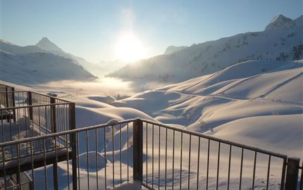 Ein wunderschöner winterlicher Ausblick mit schneebedeckten Hügeln und Bergen. Die Sonne geht langsam hinter den Bergen auf und erhellt die Szenerie.