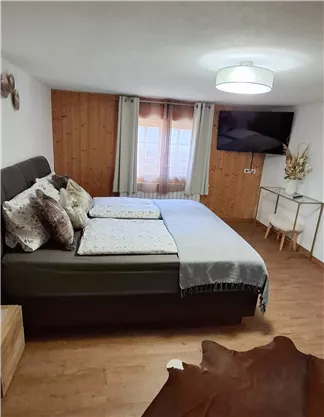 Ein gemütliches Schlafzimmer mit einem großen Bett und mehreren Kissen. Es gibt Holzwände, einen Fernseher und eine kleine Sitzecke.