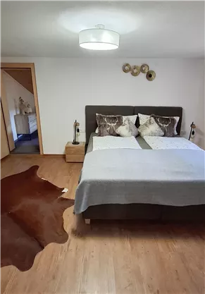 Ein gemütliches Schlafzimmer mit einem großen Bett und dekorativen Kissen. Der Boden ist mit einem Teppich aus Tierhaut ausgestattet.