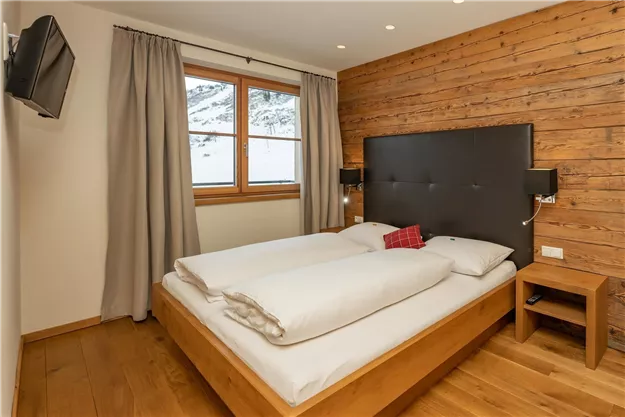 Ein modernes Schlafzimmer mit Holzverkleidung und großen Fenstern. Das Doppelbett ist gemütlich und mit weißen Bettwaren ausgestattet.