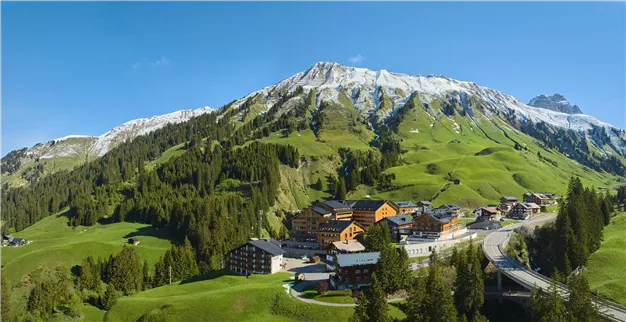 A picturesque mountain landscape with snow-covered peaks and green meadows. In the foreground, there is a charming village with traditional houses.
