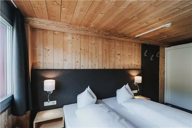 Ein gemütliches Zimmer mit zwei Einzelbetten und Holzwänden. Sanfte Beleuchtung sorgt für eine entspannte Atmosphäre.
