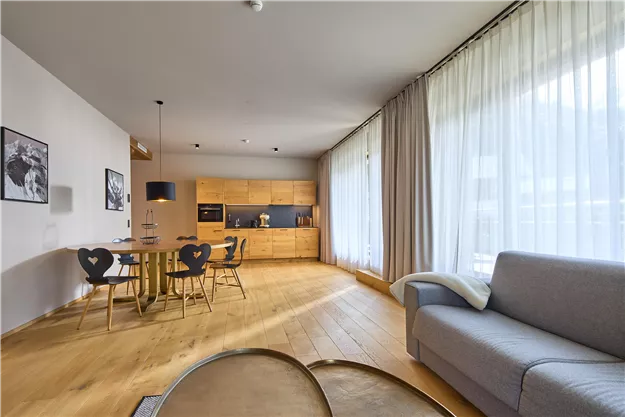 A modern apartment with hardwood floors and large windows. The dining area and kitchen are bright and invitingly furnished.