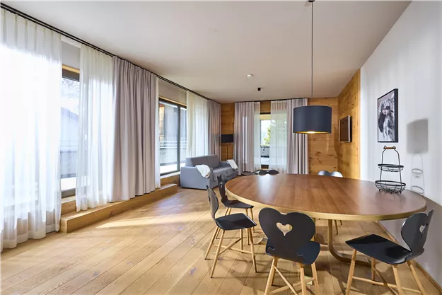 A modern dining room with a round wooden table and chairs. Large windows provide plenty of light and an open atmosphere.