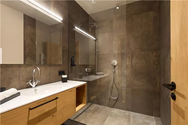 A modern bathroom with a shower and an elegant wooden drawer. The walls are in neutral tones, and there are large mirrors.