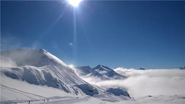 An impressive winter mountain landscape with snowy peaks and radiant sunshine. Fog drifts over the valleys, giving the scene a mystical atmosphere.